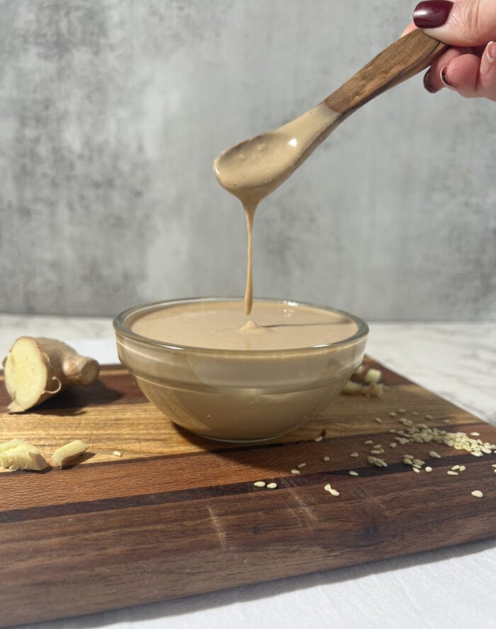 A close up of a spoon of creamy sesame ginger dressing drizzle over a bowl.