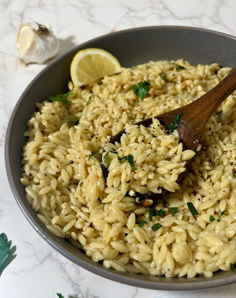 close up picture of creamy orzo in a bowl with lemon