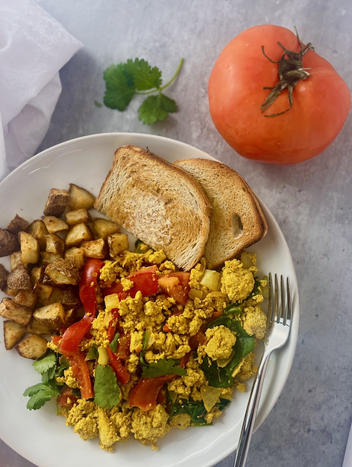 This is a picture of curry tofu scramble with a tomato and cilantro. 