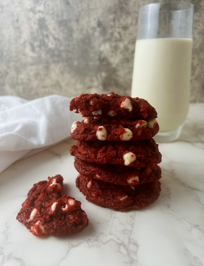 This is a picture of a stack of red velvet cookies with a glass of milk.