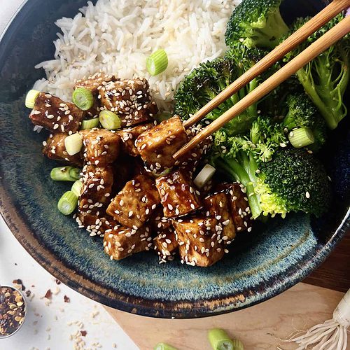 This is a photo of a bowl of sticky tofu with sesame seeds and a stir fry.