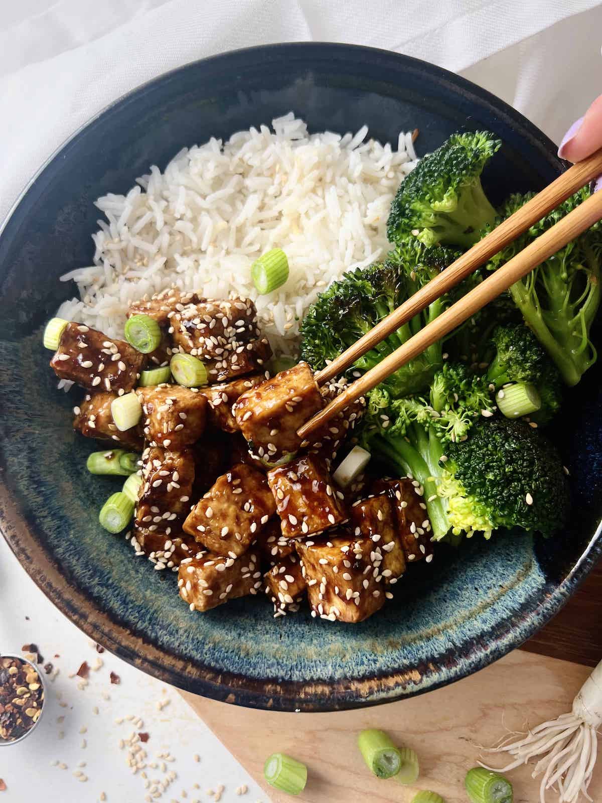 This is a photo of a bowl of sticky tofu with sesame seeds and a stir fry. 