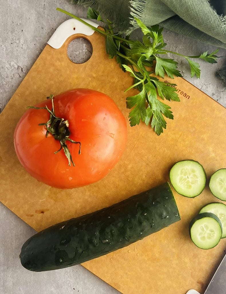 This is a photo of a large tomato with a cucumber partially diced.