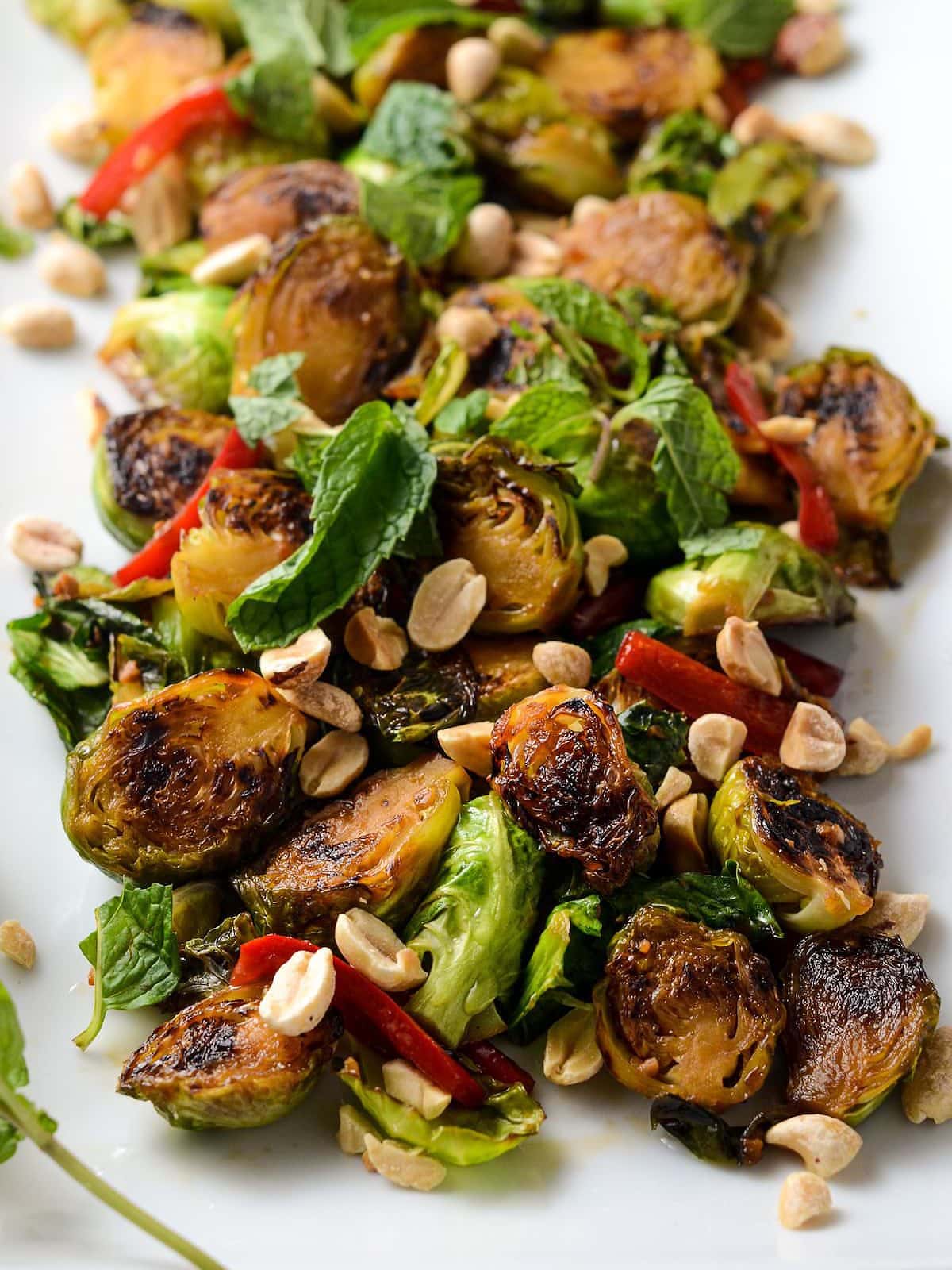 This is a photo of thai brussel sprouts on a white plate with peanuts and mint.