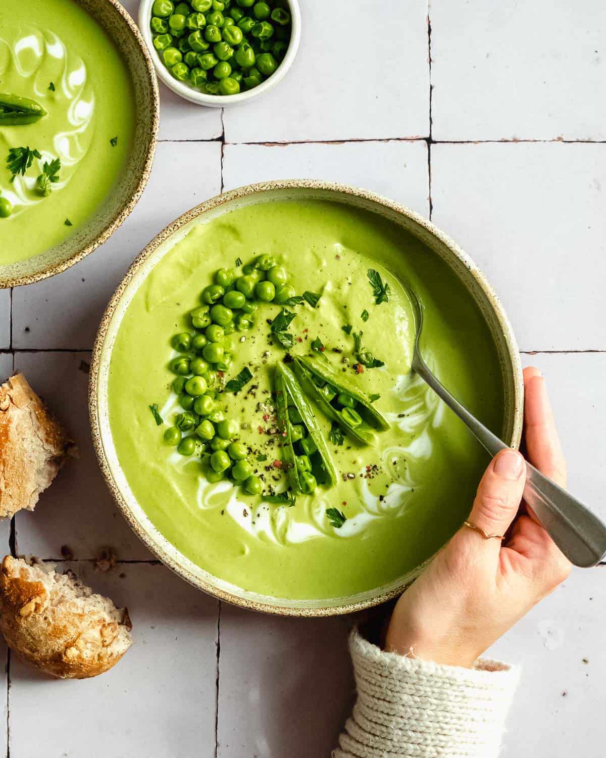  a bowl of broccoli pea soup with a hand holding the soup.