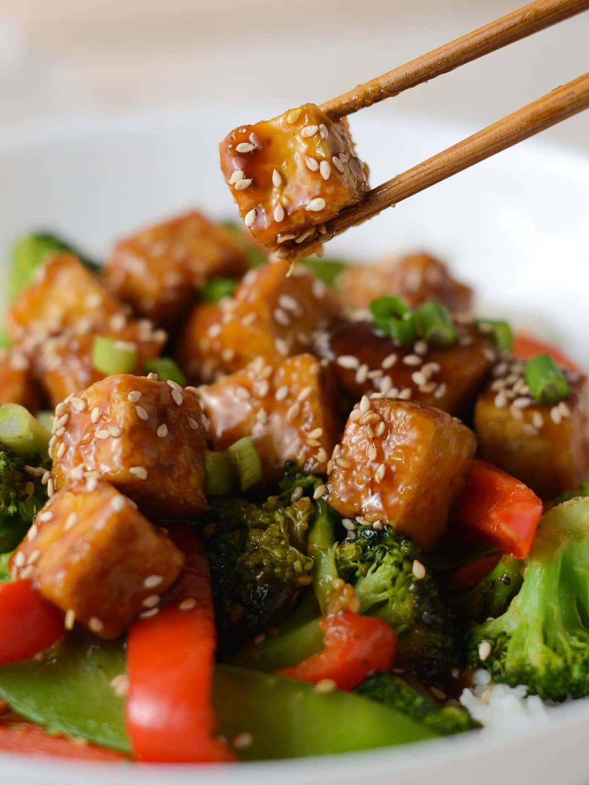 This is a photo of a chopstick holding a piece of teriyaki tofu.