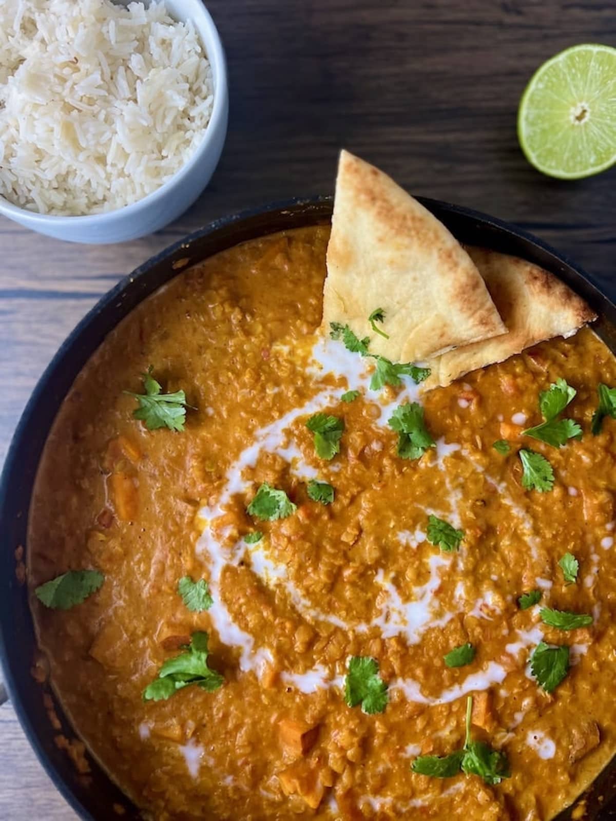 This is a photo of the curry with a piece of naan, rice, and a lime.