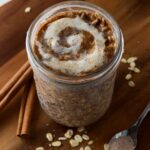 This is a photo of cinnamon roll overnight oats with a spoon and cinnamon sticks.