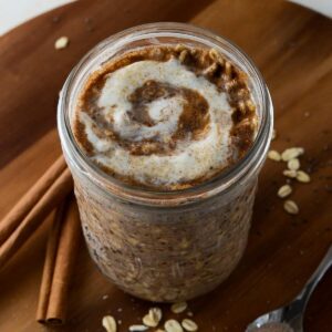 This is a photo of cinnamon roll overnight oats with a spoon and cinnamon sticks.