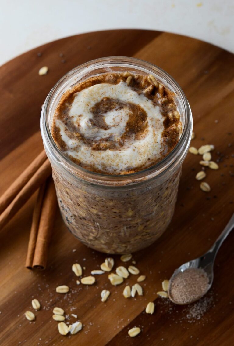 This is a photo of cinnamon roll overnight oats with a spoon and cinnamon sticks.