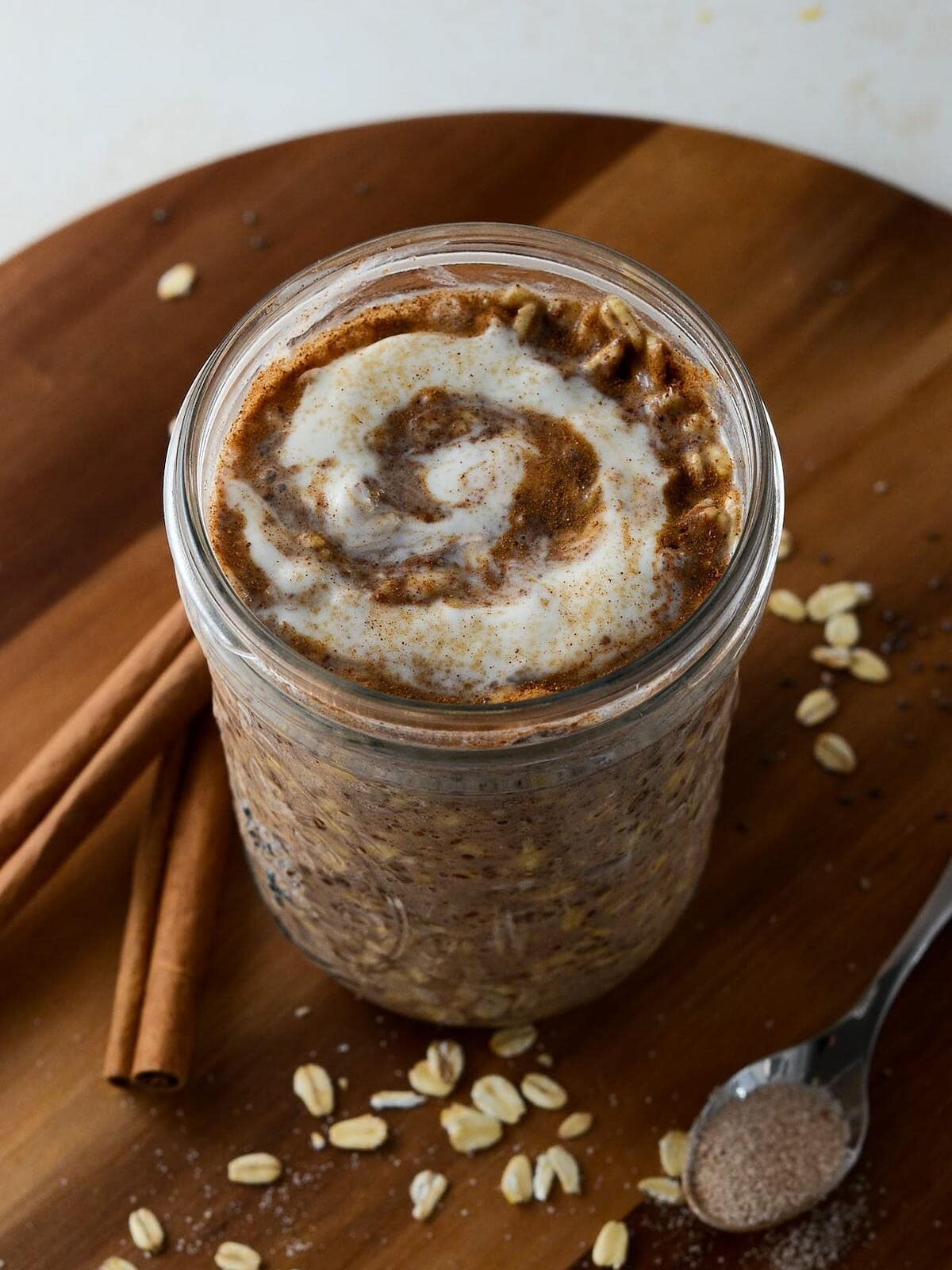 This is a photo of cinnamon roll overnight oats with a spoon and cinnamon sticks.