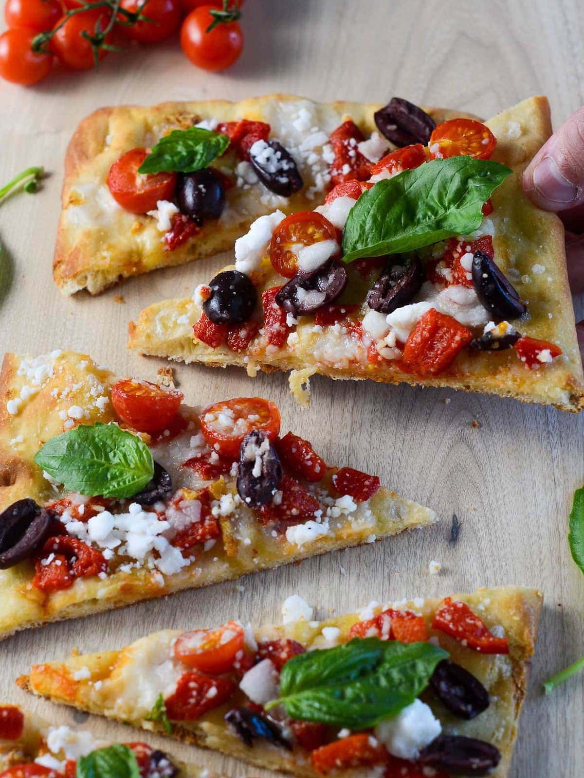 vegan flatbread pizza with a hand picking up the pizza.
