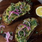 overhead shot of avocado toast with pickled onions and a lemon on the side
