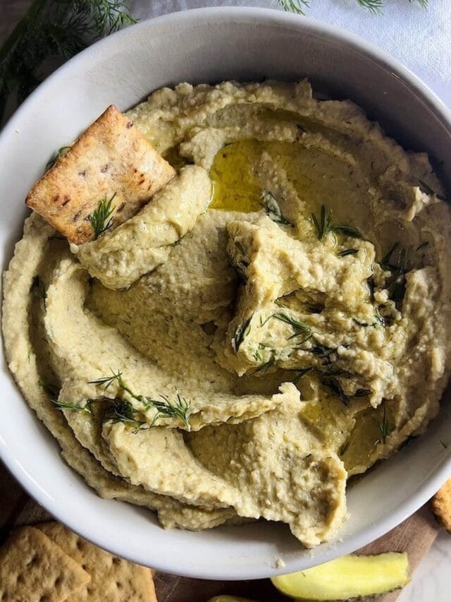 a bowl of creamy dill pickle hummus with a pita cracker