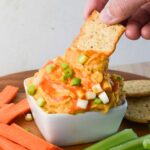 buffalo chickpea dip with a cracker and a hand