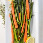 carrots and asparagus on a large rectangular plate with lemons and thyme on the side.