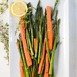carrots and asparagus on a large rectangular plate with lemons and thyme on the side.