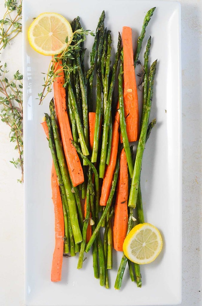carrots and asparagus on a large rectangular plate with lemons and thyme on the side.