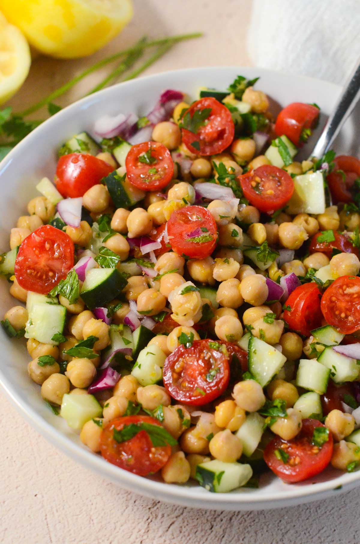 chickpea salad in a bowl with a spoon and a lemon in the background.