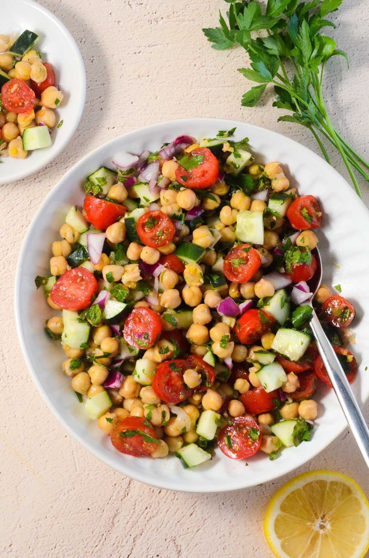 picture of chickpea salad in a bowl with parsley in the upper right corner and some salad on a small plate on the side.