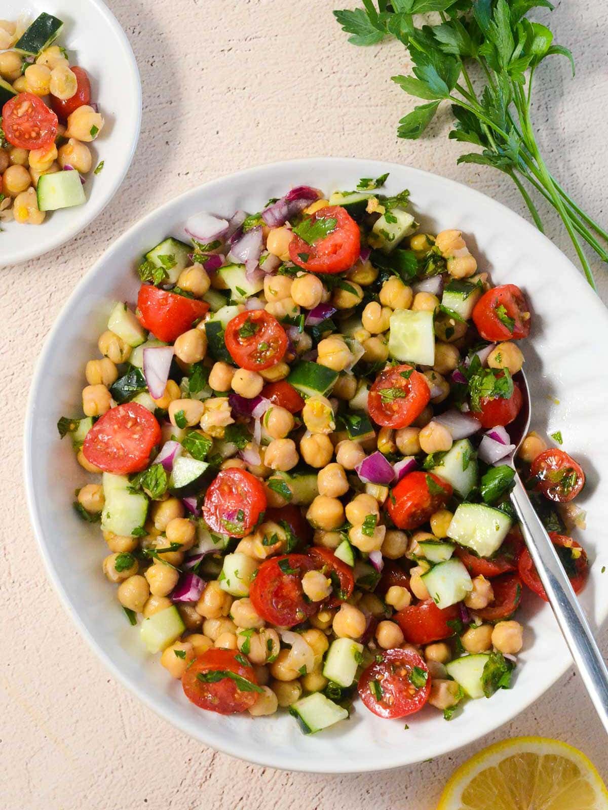 picture of chickpea salad in a bowl with parsley in the upper right corner and some salad on a small plate on the side.