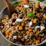fall farro salad in a bowl with a large spoon and parsley.