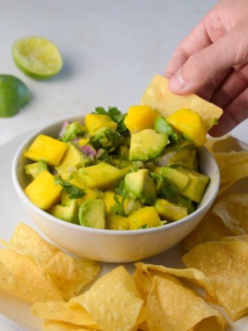 a chip dipping into the mango avocado salsa.
