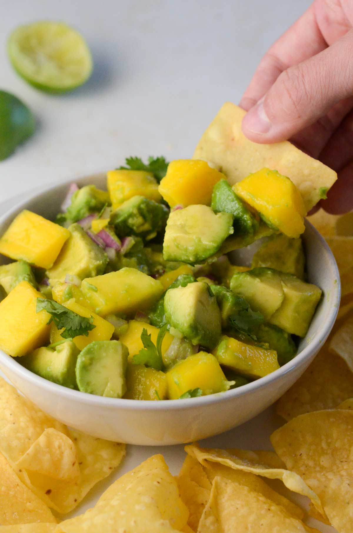 mango avocado salsa in a bowl with a hand dipping a chip in it.