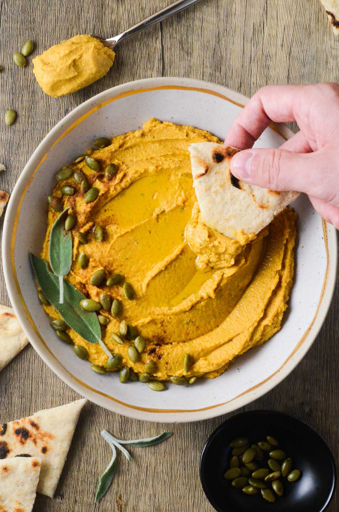 pumpkin hummus in a bowl with a hand dipping pita into it.