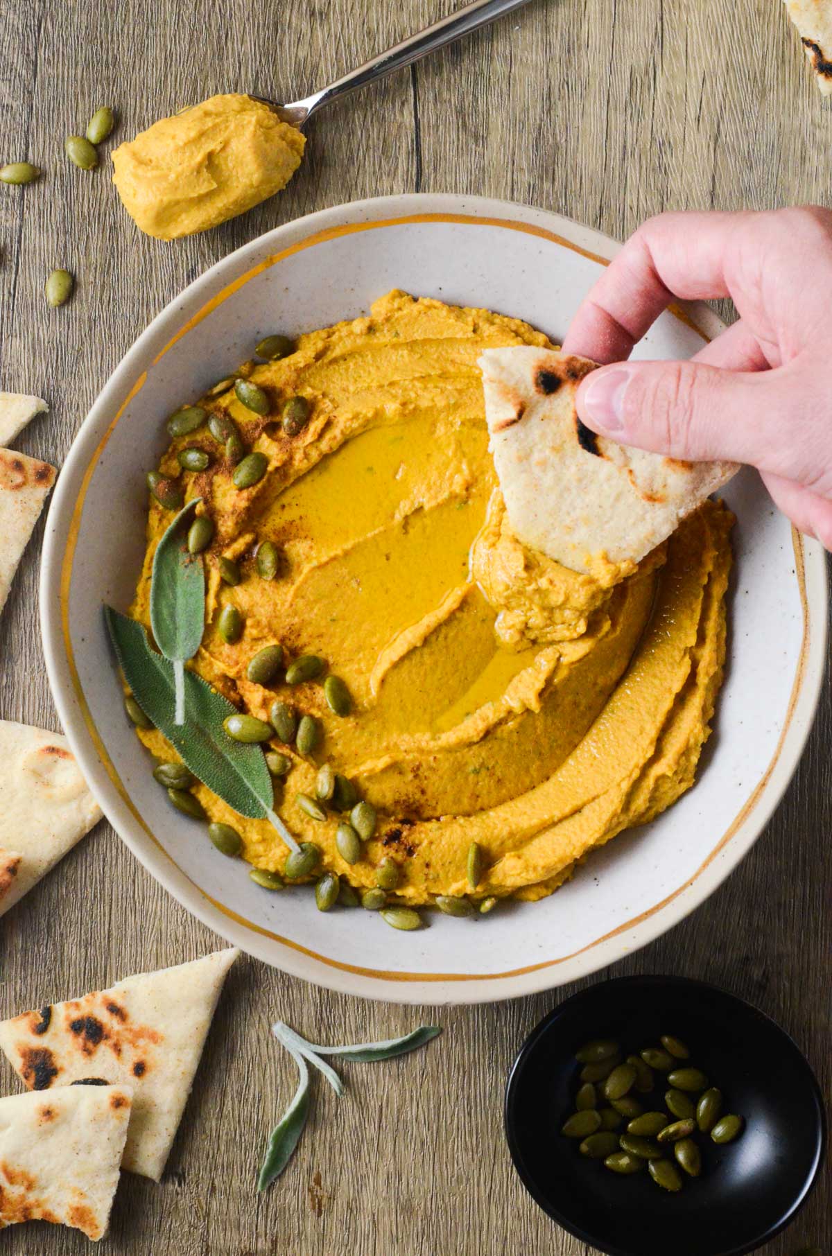 a photo of pumpkin hummus with a pita dipping into it. 