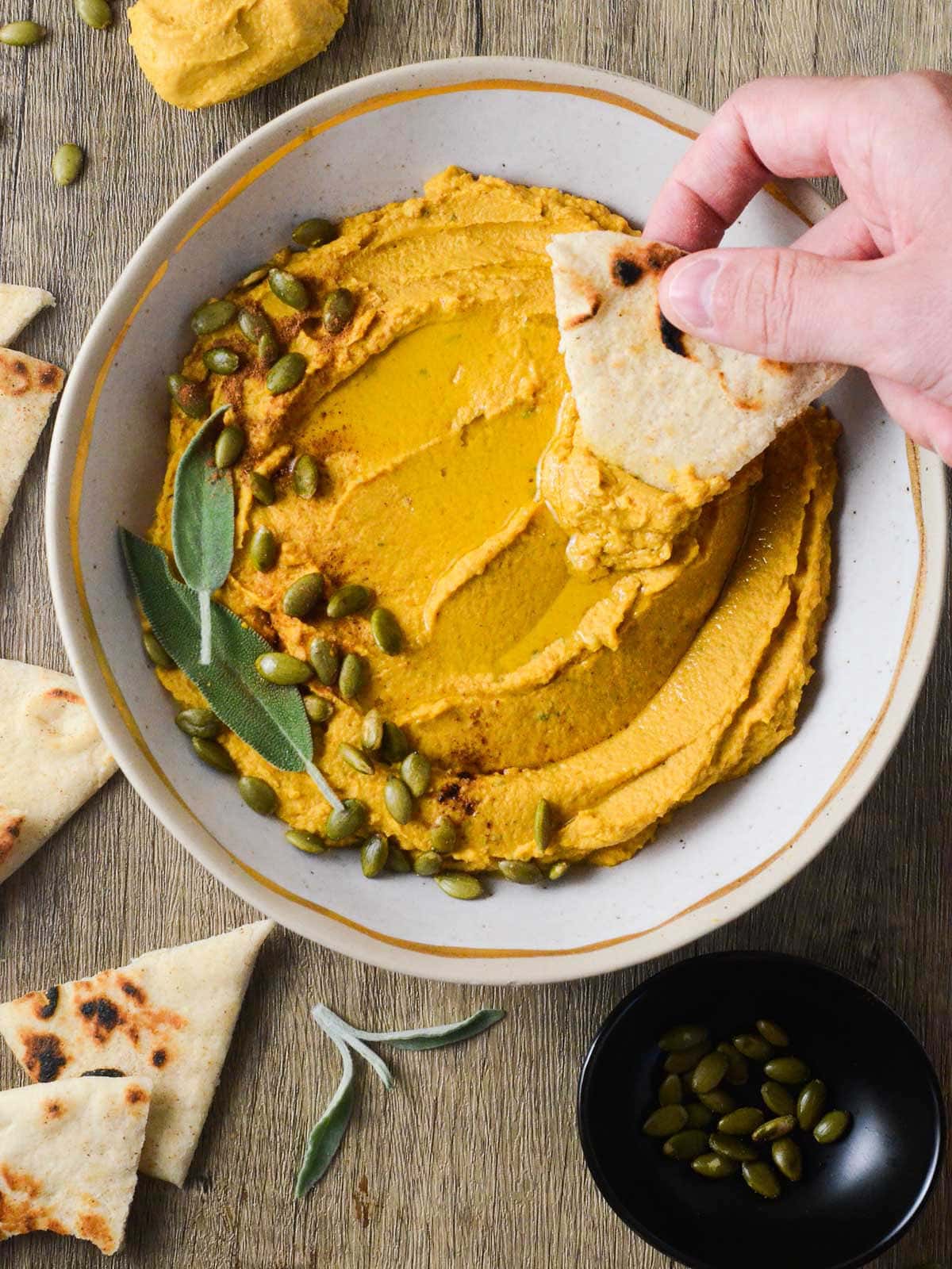 a photo of pumpkin hummus with a pita dipping into it. 