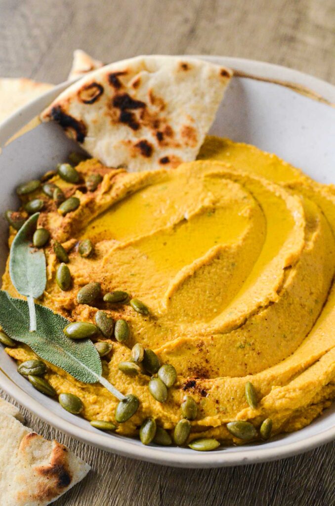 pumpkin hummus in a bowl with a pita dipped into it.