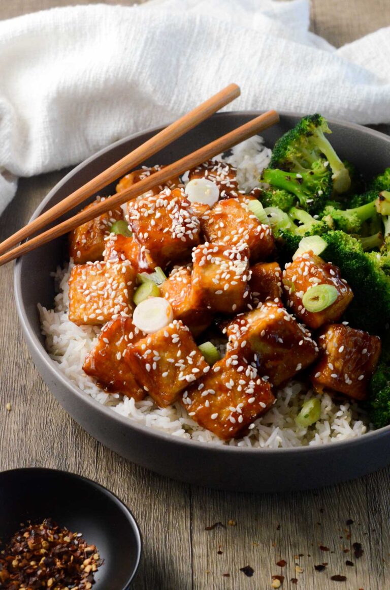 bowl of sticky tofu with chopsticks, rice, and broccoli.