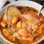 a bowl of gnocchi soup with bread in a it and basil.