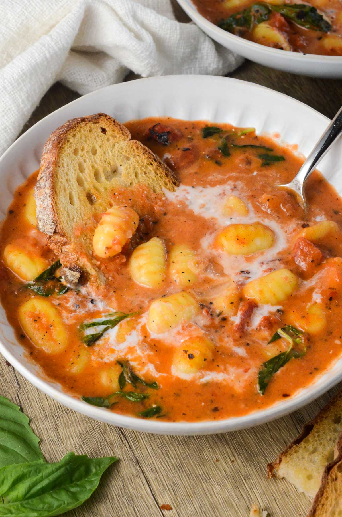 a bowl of gnocchi soup with bread in a it and basil. 