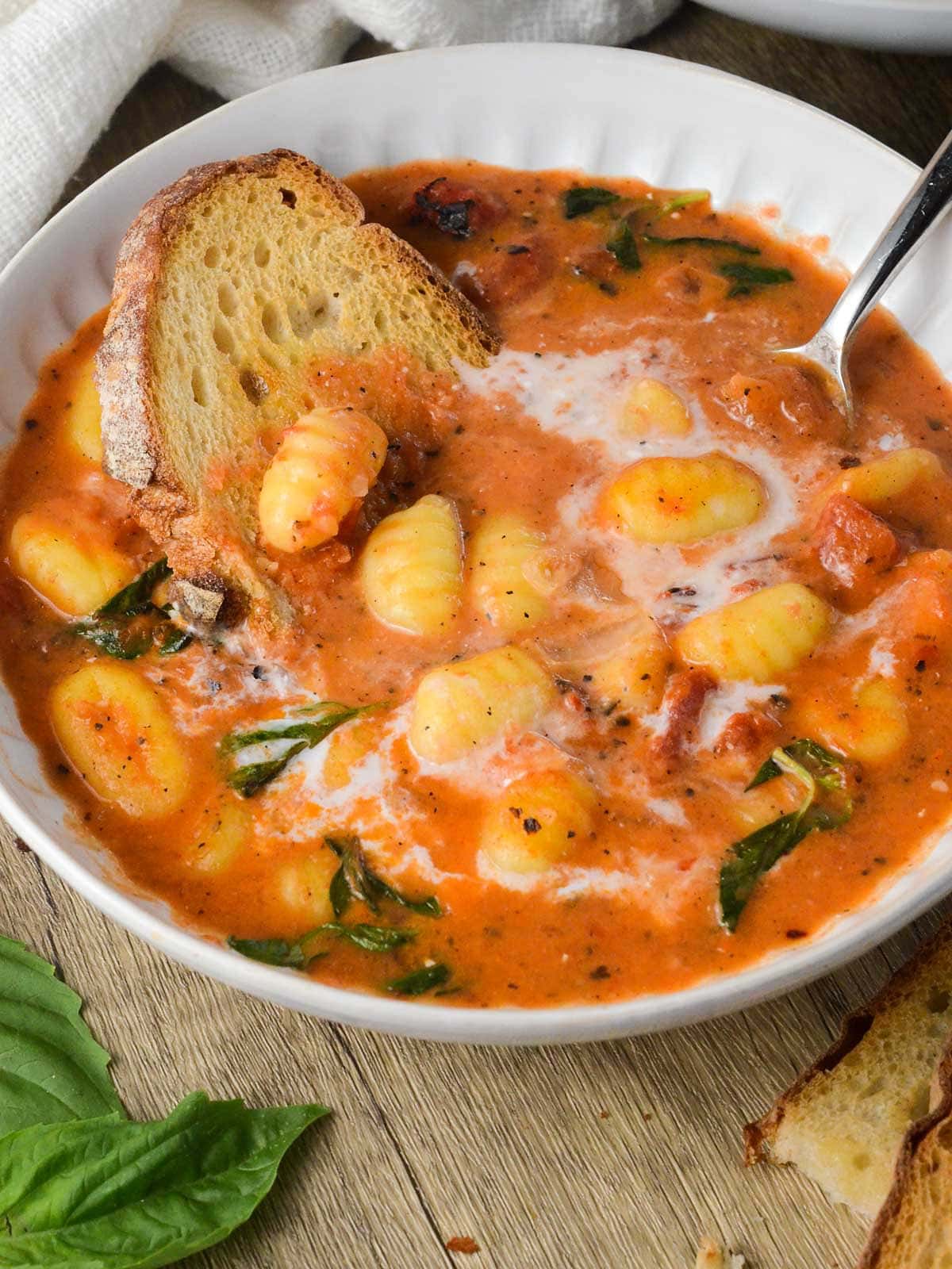 a bowl of gnocchi soup with bread in a it and basil. 