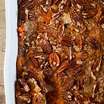 the vegan sweet potato casserole in a large casserole dish with a spoon scooping into it.