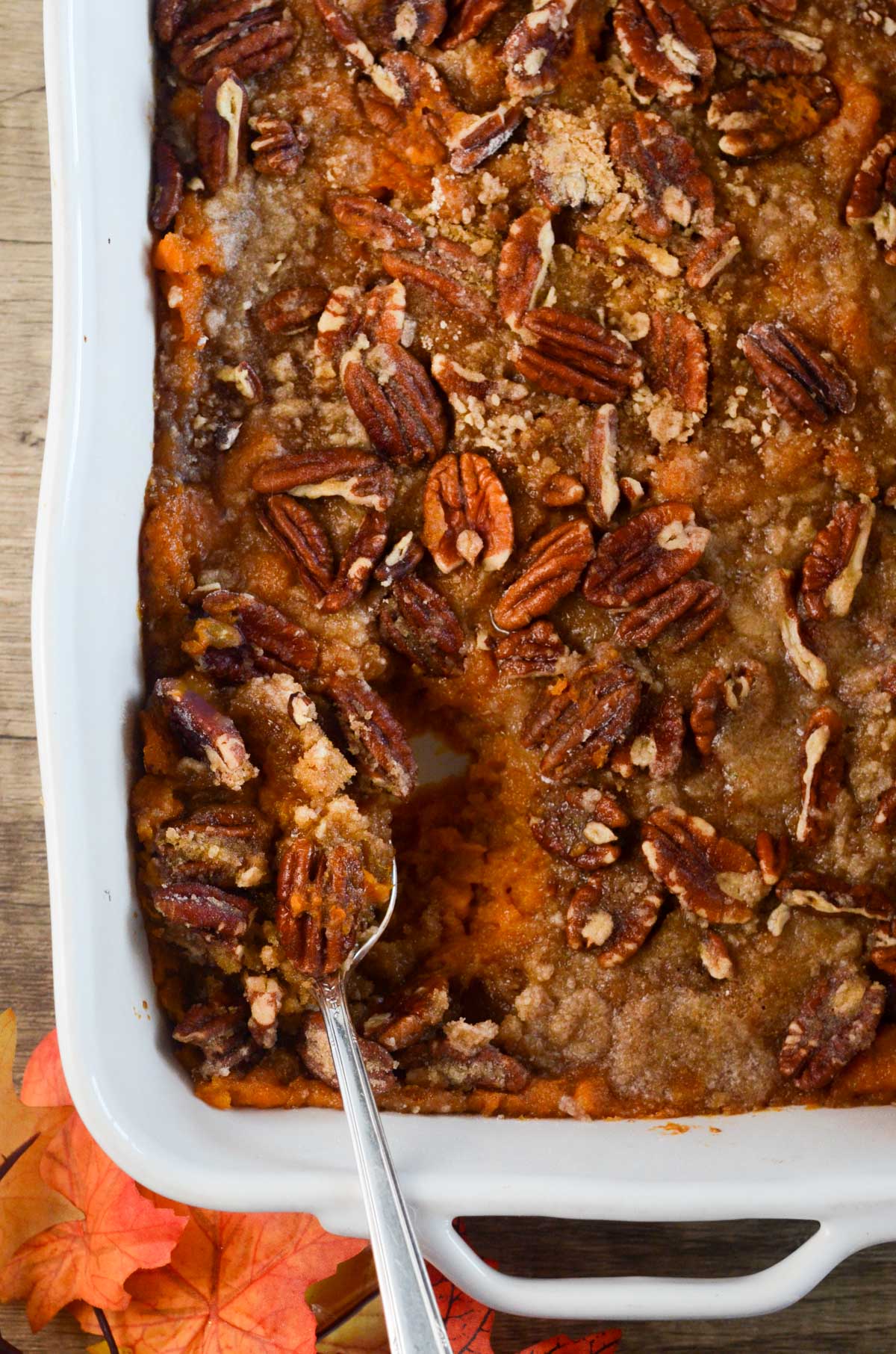 the vegan sweet potato casserole in a large casserole dish with a spoon scooping into it.
