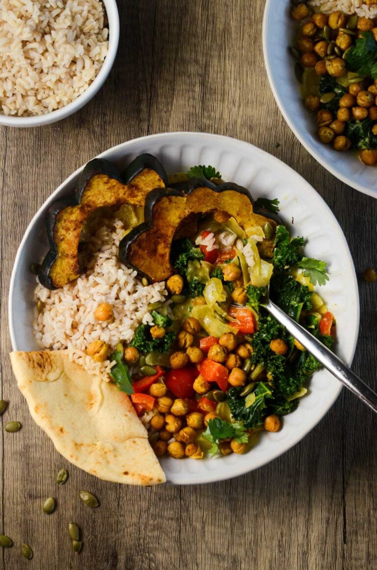 a spoon and piece of naan in a bowl of acorn squash curry.