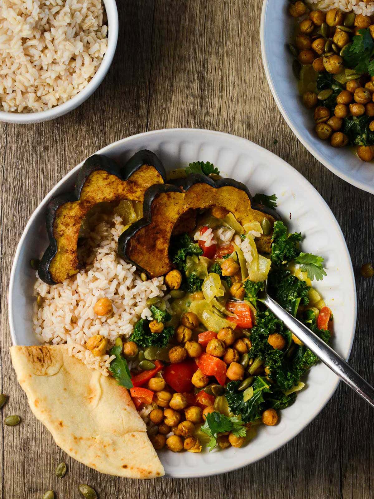 a spoon and piece of naan in a bowl of acorn squash curry.