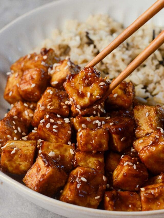 crispy asian tofu with sesame seeds on top and a chopstick picking it up.