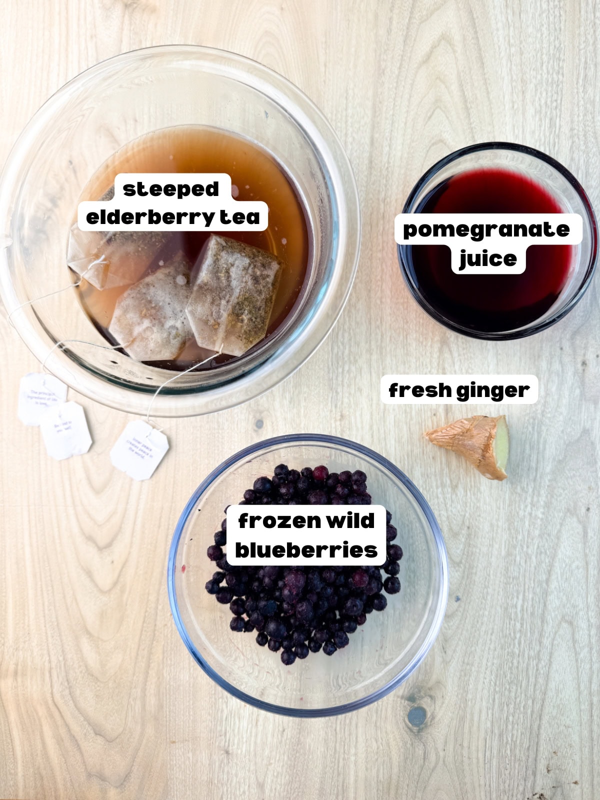 ingredients for the elderberry immunity shots including elderberry tea, fresh ginger, pomegranate juice, and frozen wild blueberries